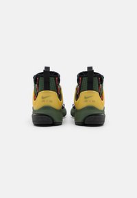 Tenisky Nike Air mají zeleno-žlutý design s texturovaným textilním svrškem a černou gumovou podrážkou. Zajímavé červené zipy na zadní straně.