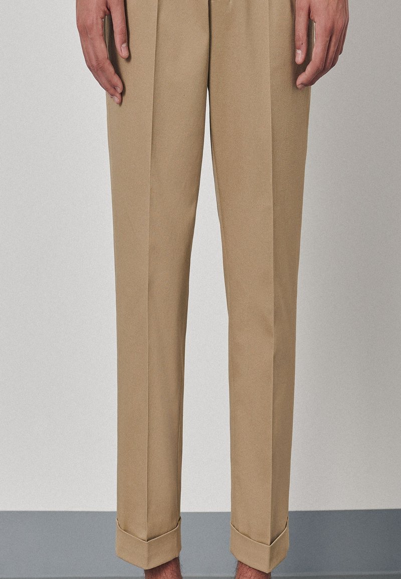 Pantalon kaki à coupe fuselée, avec une texture lisse et des revers roulés, présenté sur un fond neutre.