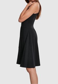 Svart ärmlös klänning med figurnära bodice och utställd kjol, tillverkad av ett slitstarkt tyg; knälängd med en ren, minimalistisk design.