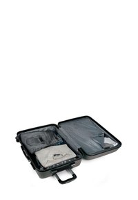 Maleta negra abierta con ropa doblada en su interior, incluyendo jeans grises, un suéter claro y otras prendas, sobre un fondo blanco.