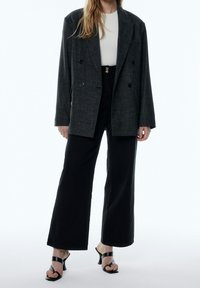 Blazer gris de doble botonadura, top blanco entallado, pantalones negros de pierna ancha y sandalias de tacón negras. Tela texturizada con un corte a medida.