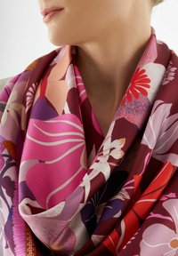Foulard en soie floral dans des teintes de rose, rouge et violet, présentant une variété de fleurs et des motifs abstraits ; texture lisse et tombe élégamment.