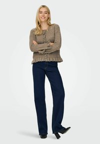 Hellbrauner Strickcardigan mit Knöpfen, gerüschtem Saum und langen Ärmeln, kombiniert mit dunkelblauen weiten Jeans und schwarzen High Heels.