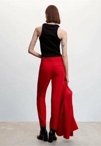 Pantalon rouge ajusté avec une coupe slim, associé à un haut sans manches noir. Les détails notables comprennent une taille haute et un tissu lisse.