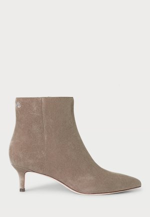 Botte de cheville en daim gris avec un bout pointu et un petit talon, présentant un détail de logo près du haut et une surface lisse et texturée.