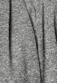 Grå stickad tyg med ett texturerat mönster som innehåller en blandning av ljusa och mörka fibrer, vilket skapar en melerad effekt.