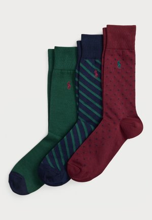 Trois paires de chaussettes pliées mi-mollet en vert, bleu marine avec des rayures vertes, et bordeaux avec des pois navy, chacune ornée d'un petit logo brodé.