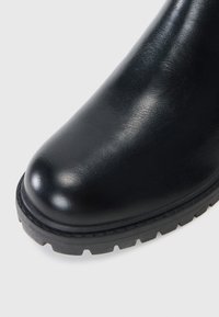 Bota de cuero negro con punta redondeada, parte superior texturizada y suela de goma resistente con un patrón de relieve profundo para mayor agarre.