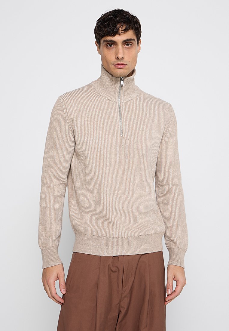 Beige Rippenstrickpullover mit hohem Reißverschlusskragen, langen Ärmeln und taillierter Passform. Hergestellt aus weichem Material mit strukturierter Oberfläche.