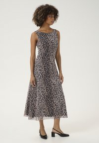 Rochie fără mâneci cu imprimeu de leopard în nuanță de bej și pete negre, design în formă de A evazat, material neted și lungime până la genunchi. Stilizată cu pantofi cu toc deschis negri.