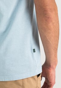 Hellblaues Baumwoll-T-Shirt mit kurzen Ärmeln, Seitennähten etikettiert und schlichter Textur. Sichtbare Nähte entlang des Saums und der Ärmelsäume.