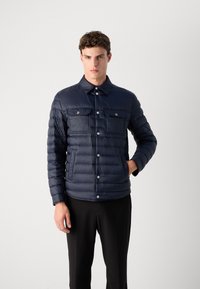 Mornarska puffer jakna z gumbnim zapiranjem spredaj, dvema žepoma na prsih in klasičnim ovratnikom. Ima prešito teksturo in prilegajoč silhueto.