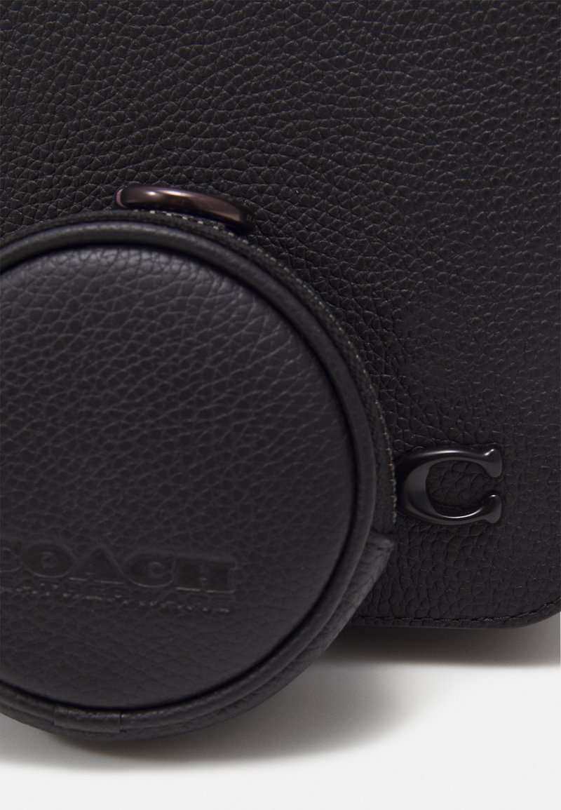 Schwarze Lederhandtasche mit strukturiertem Oberflächen, ausgestattet mit einem runden Münzfach und einem dezenten geprägten Logo. Dunkle Metallakzente ergänzen das Design.