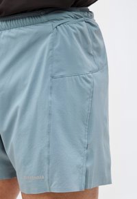 Ανοιχτό μπλε σορτς με ελαστική μέση και πλαϊνή τσέπη, φορεμένα από ένα άτομο πάνω σε απλό λευκό φόντο.