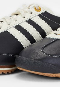 Navy leather sneakers with cream stripes and laces, featuring a textured black toe cap and a gum rubber outsole with serrated grip patterns.