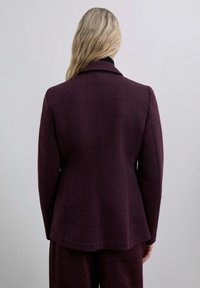 Blazer burdeos con un patrón a cuadros, con un corte ajustado, solapas de muesca y una textura suave. Visto desde la parte trasera.