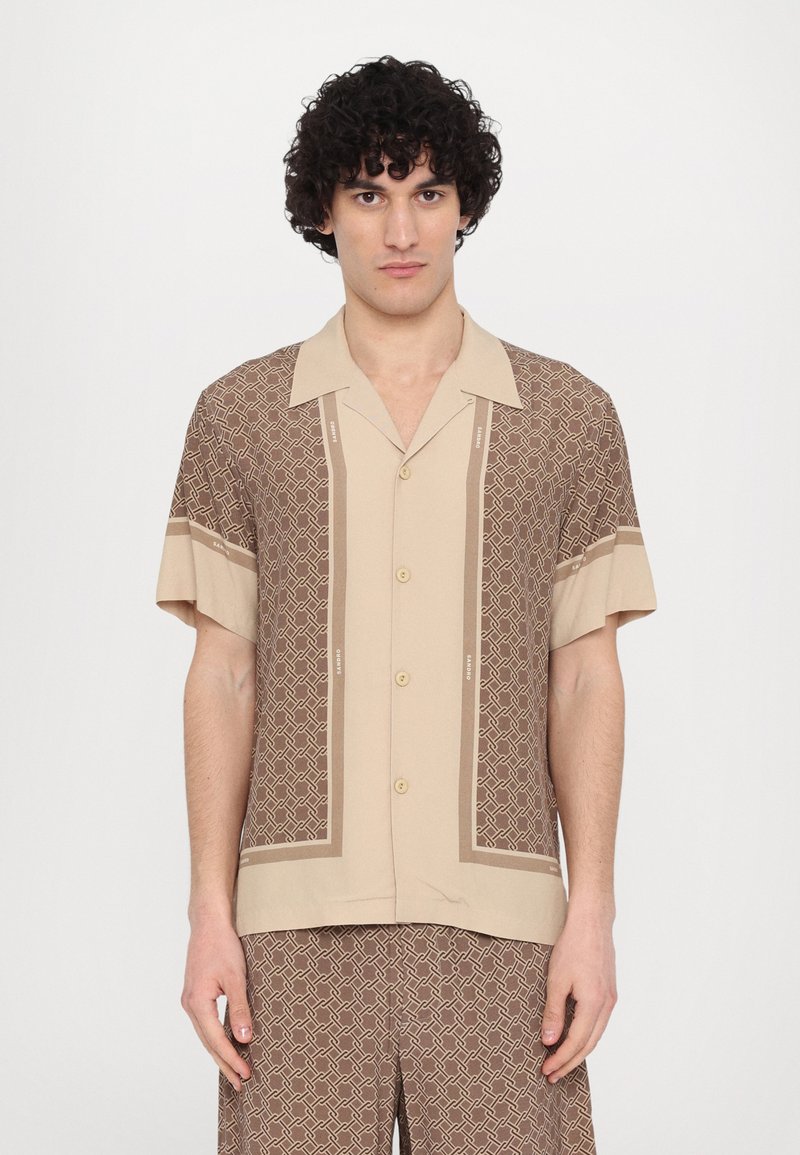 Chemise beige à manches courtes avec des motifs géométriques marron et une fermeture à boutons sur le devant. Texture lisse avec des rayures contrastantes sur les manches.