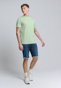 Lichtgroen katoenen t-shirt met korte mouwen, gecombineerd met denim shorts met omgeslagen mouwen en witte sportschoenen met grijze accenten.