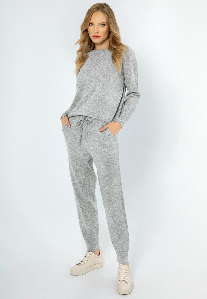 Grijs gebreid loungewear-set met een langemouwtop en tapered broek met een koord in de taille, gecombineerd met lichte sneakers.