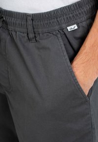 Graue Shorts aus Baumwolle mit elastischem Bund und Seitentaschen. Ein kleines weißes Etikett mit "Rell" ist am Bund sichtbar.