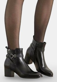Bottines en cuir noir avec fermeture éclair, accents texturés, détail de boucle et talon épais. Fini de surface lisse.