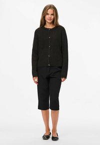 Cardigan en tricot foncé avec col rond et fermeture à cinq boutons, associé à un pantalon noir court et des ballerines noires. Texture lisse sur l'ensemble.