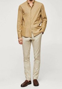 Camicia a bottoni gialla chiara con righe verticali, abbinata a pantaloni beige. Mocassini marroni completano l'outfit.