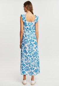 Vestido maxi con un patrón floral azul sobre fondo blanco, con tirantes de hombro con volantes y una espalda descubierta, hecho de una tela ligera.