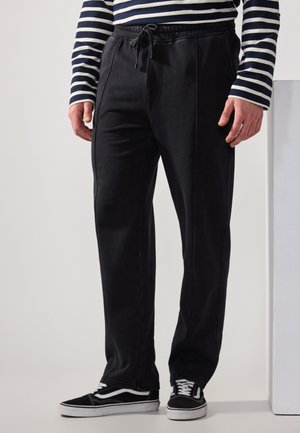 Pantalones de chándal negros con cintura elástica y cordón. Presentan costuras laterales, piernas rectas y un tejido suave y liso. Se llevan con zapatillas negras.