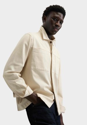 Lysebeige skjorte med knapper, krave og to forlommer, lavet af et blødt stof. Har opviklede manchetter og en afslappet pasform.