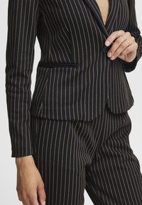 Navy striped suit with thin gold lines, tailored fit, single-button closure, and a notch lapel. Features a side pocket detail.