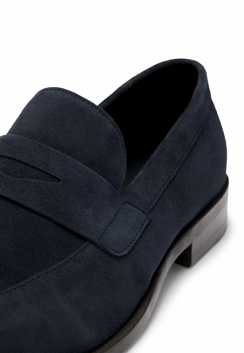 Loafer en suede bleu marine avec une surface lisse, un bout rond et un détail cousu sur le devant. Présente un petit talon en bois.