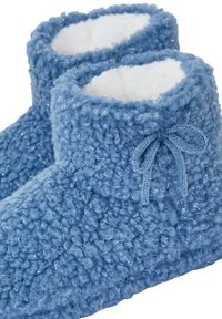 Miękkie, niebieskie dzianinowe buciki dla niemowląt z białym puszystym wykończeniem i małą dzianinową kokardką na przedniej stronie, prezentowane pod kątem na białym tle.
