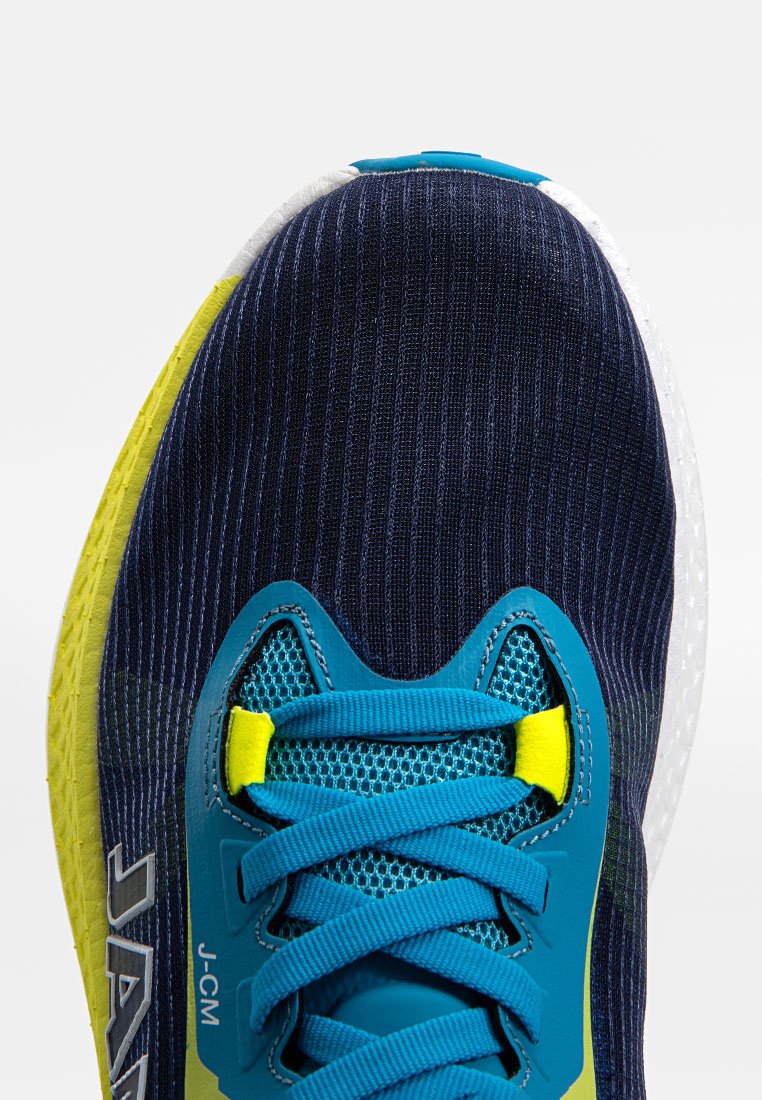 Zapatilla atlética en azul marino y amarillo con una parte superior de tela texturizada, cordones azules y una suela exterior con un patrón único. Destacada marca J-CM en el lateral.