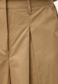 Beige broek met een gladde textuur, middelhoge taille, voorpincette details en zijzakken. Gemaakt van lichtgewicht stof.