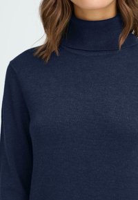Marinblå turtleneck-tröja med ribbat krage, tillverkad av mjukt stickat material, med en slät yta och figurnära passform.