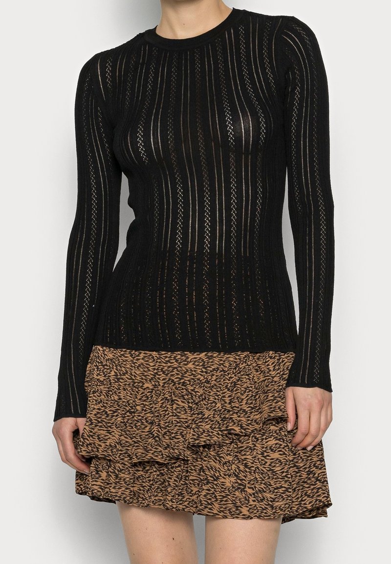 Musta pitkähihaisen yläosa, jossa on läpikuultava, ribattu rakenne ja vaakasuorat raidat, yhdistettynä ruskeaan röyhelöiseen hameeseen, jossa on hienovarainen kuvio.