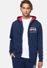 Felpa con zip color navy e fodera rossa, con un logo sul petto, tasche frontali e cordini regolabili sul cappuccio.