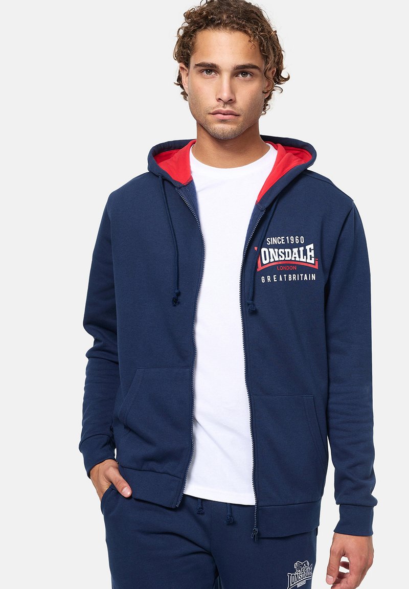 Felpa con zip color navy e fodera rossa, con un logo sul petto, tasche frontali e cordini regolabili sul cappuccio.