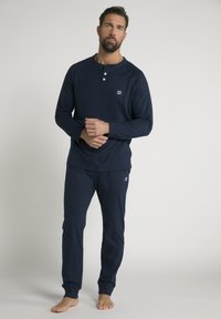 Marineblauw loungewear set met een langemouwen top met een drieknoopsluiting en bijpassende broek. Zacht materiaal, getailleerde pasvorm, minimale logo-details.