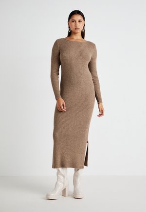 Ribbed, long-sleeve, beige dress with a boat neckline and side slit, paired with white knee-high block-heel boots. Smooth texture.