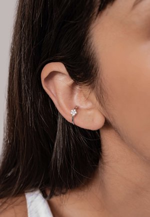 Silberne Creolen mit floralem Design, verziert mit kleinen, klaren Steinen. Am Ohr getragen, zeigen sie eine polierte Metalloberfläche.
