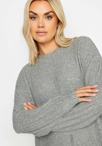 Maglione grigio a coste con maniche lunghe e scollatura rotonda. Il tessuto appare morbido con un motivo testurizzato e una vestibilità comoda.