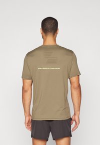 T-shirt atlético de cor verde-azeitona com mangas curtas, apresentando um design perfurado e "WORLD SERIES OF FITNESS RACING" impresso em verde claro.