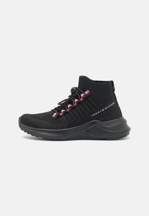 Zwarte sportieve schoen met een gebreide bovenkant, gestructureerde zijkant en elastische veters. Kenmerken zijn rode en witte accenten en een stevige zwarte zool.