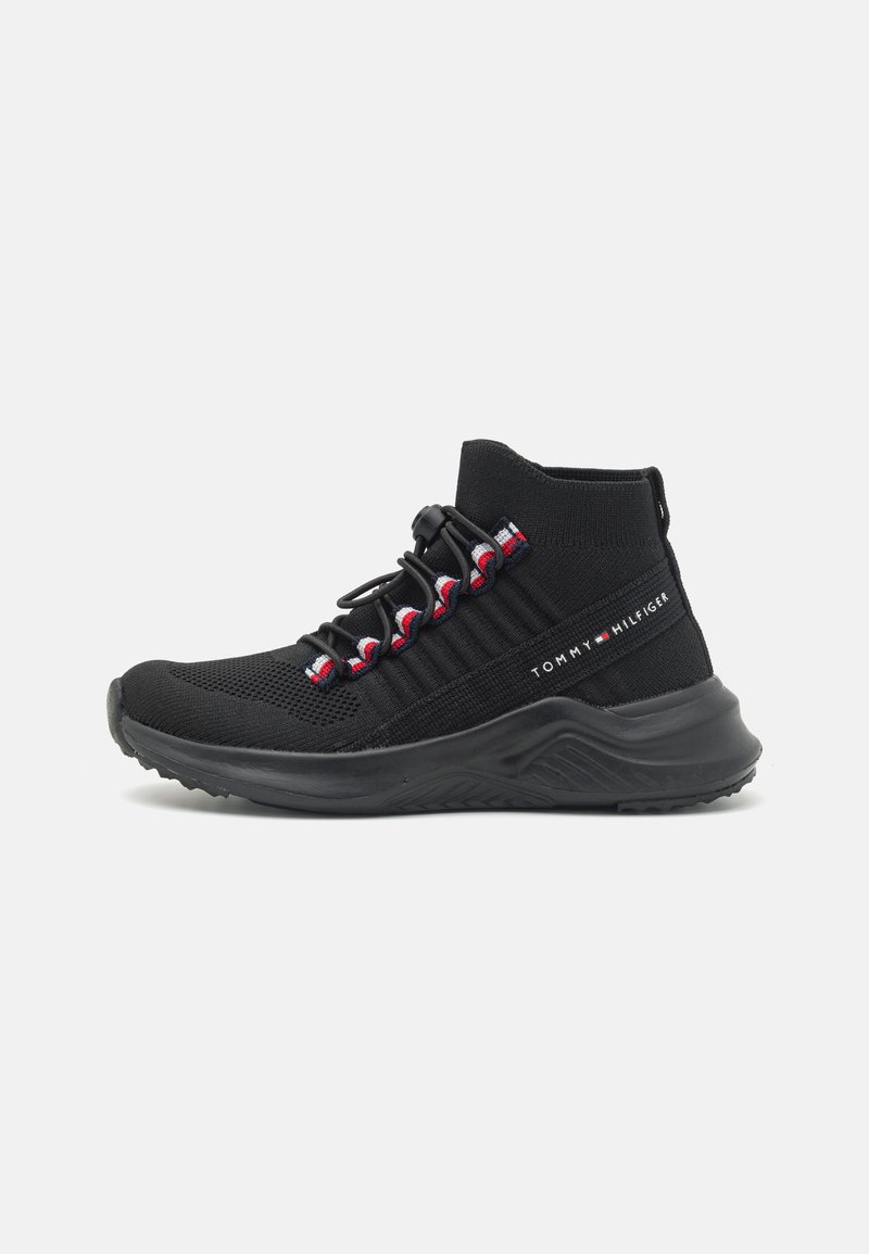 Zwarte sportieve schoen met een gebreide bovenkant, gestructureerde zijkant en elastische veters. Kenmerken zijn rode en witte accenten en een stevige zwarte zool.