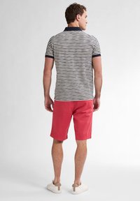 Gestreepte poloshirt in navy en wit, gecombineerd met korte rode shorts. Model draagt beige sneakers, met een minimalistisch ontwerp en pasvorm.