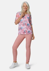 Blusenshirt mit kurzen Ärmeln in floralen Mustern in Pink, Blau und Weiß, kombiniert mit figurschmeichelnden rosa Hosen und weißen Turnschuhen. Weicher Stoff und lässige Passform.