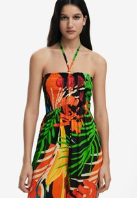 Vestido sin tirantes con un corpete ajustado y fruncido y una falda fluida. Impresión tropical audaz con rojo, verde y naranja sobre un fondo negro.