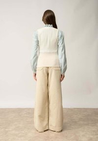 Kremowy dzianinowy kamizelka nałożona na jasnoniebieską koszulę z długim rękawem, zestawiona z szerokimi, prążkowanymi beżowymi spodniami. Subtelna tekstura i warstwowy design.